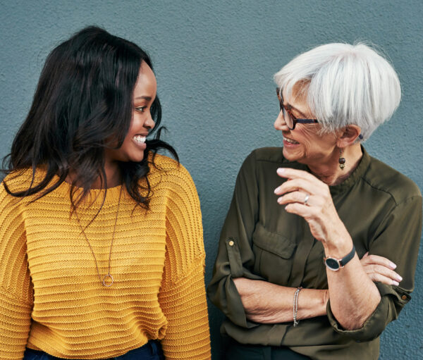 Shot of two cheerful businesswomen having a discussion while standing against a wall outdoors