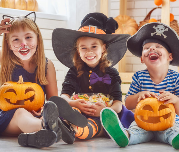 Happy brother and two sisters on Halloween. Cheerful children play with pumpkins and candy.